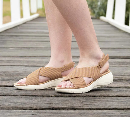 Woman wearing tan comfort sandals with crisscross straps on a wooden bridge