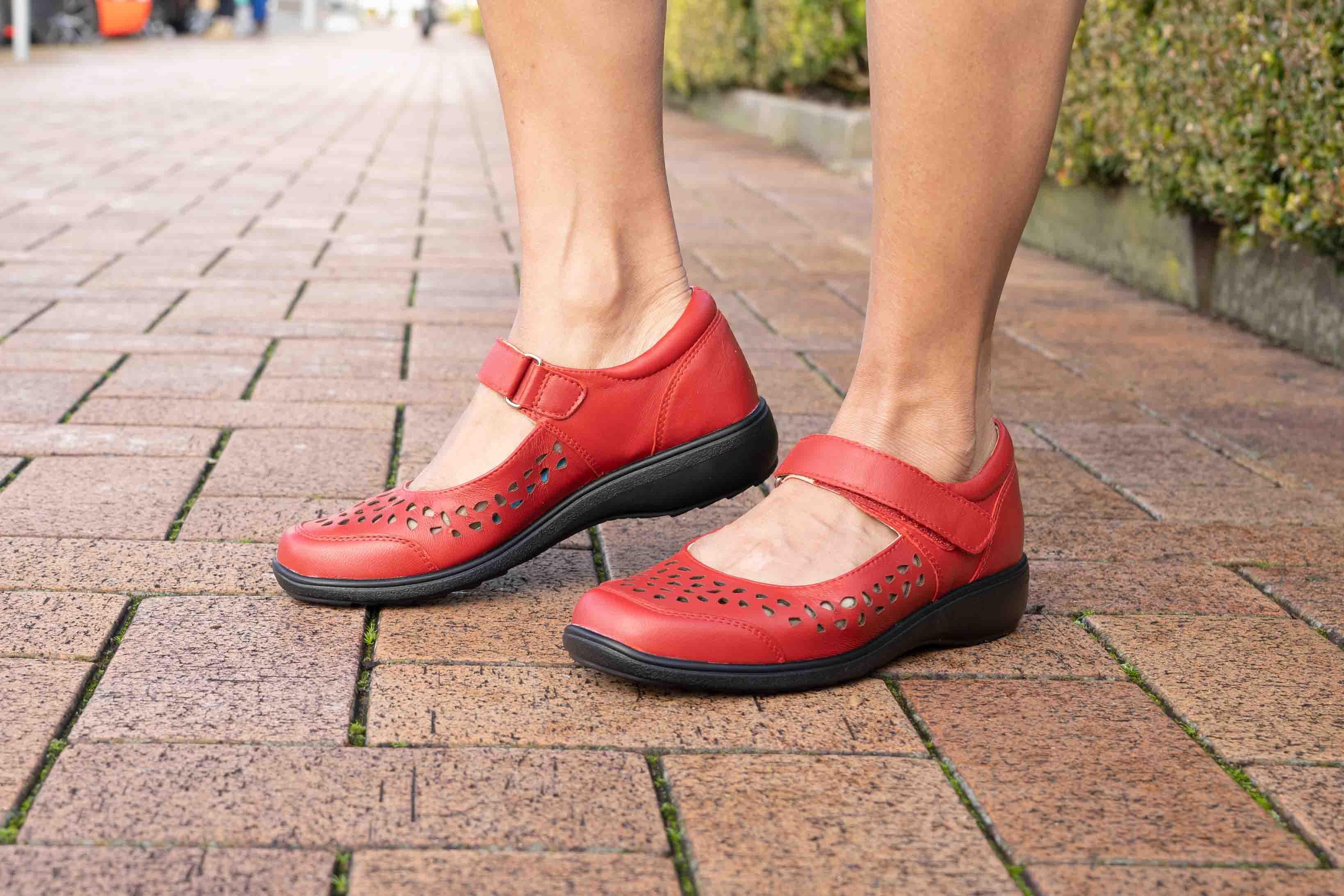 Red Mary Jane comfort walking shoes with perforated design worn outdoors on brick pavement